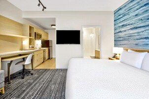 Une chambre d’hôtel avec un grand lit, un bureau avec une chaise, une télévision et une salle de bain visible à travers une porte ouverte.