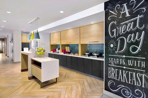 Une cuisine moderne dotée d’un îlot central, de meubles en bois et d’un tableau noir sur lequel est écrit : « Une belle journée commence par un bon petit-déjeuner ».