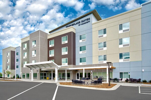 Un hotel de varios pisos con entrada cubierta, mobiliario exterior y estacionamiento.