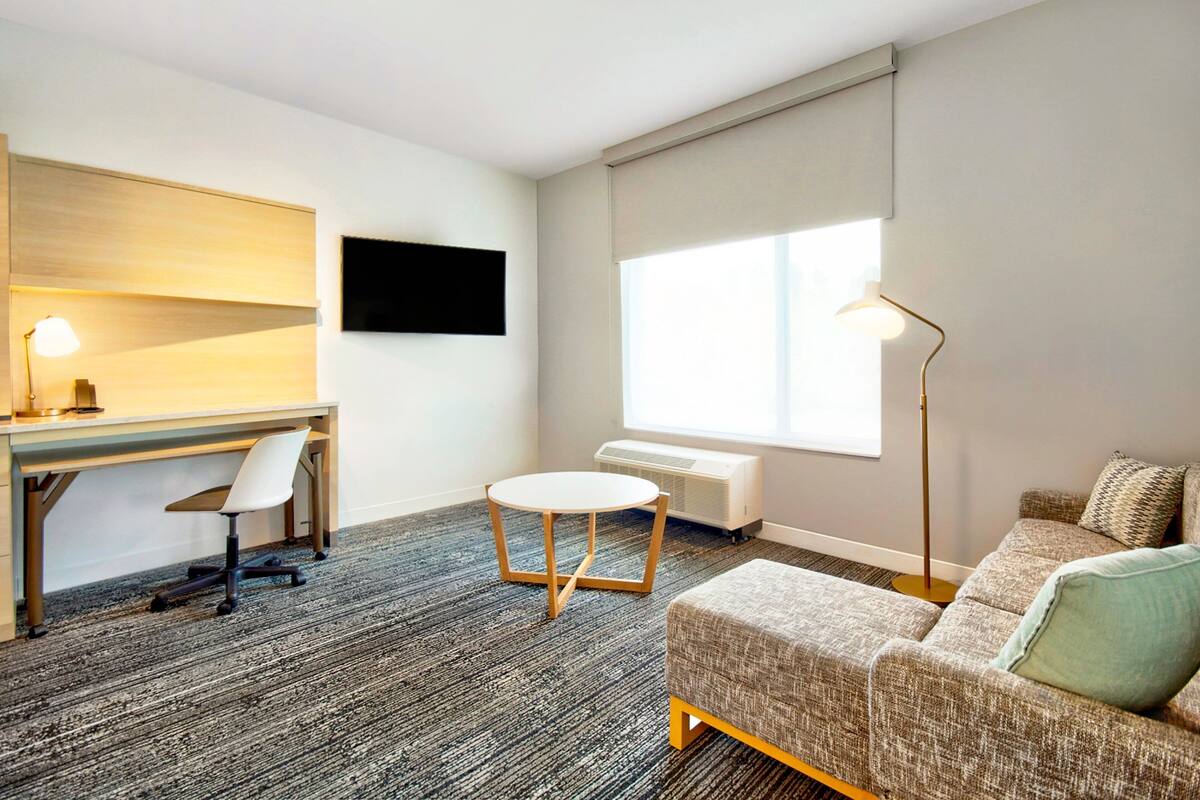 Ein modernes Hotelzimmer mit Schreibtisch, Stuhl, Sofa und einem großen Fenster.