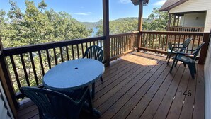 A wooden deck with a round table and chairs, overlooking a lake and forested hills.