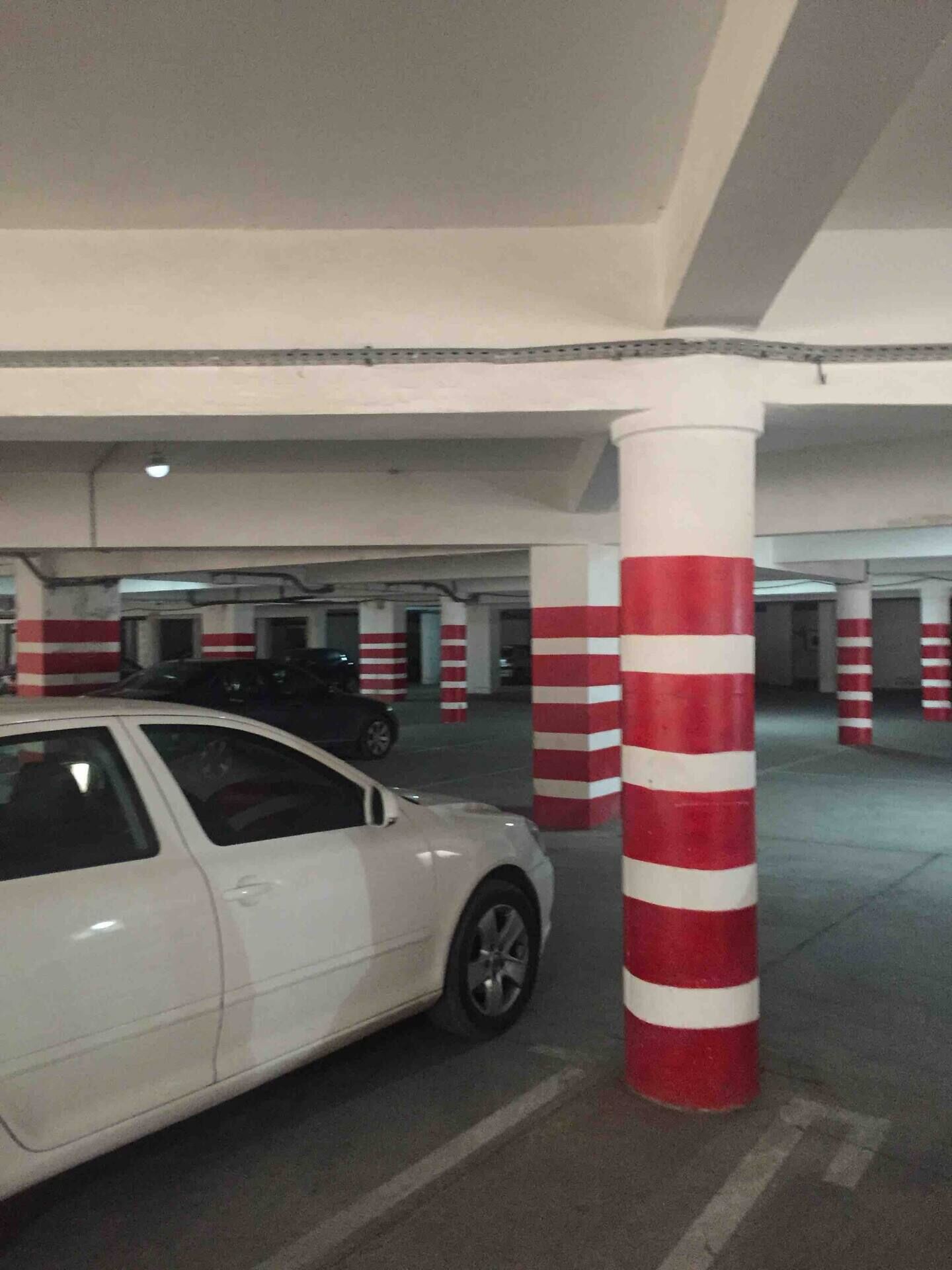 En parkeringskælder med hvide og røde stolper, en hvid bil parkeret på en plads, og flere parkeringspladser.