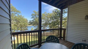 A covered porch with a view of a lake, two green chairs, and a table. - Rock Lane 150 lakefront with resort amenities! (Branson)
