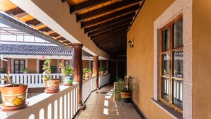 A covered corridor with tiled flooring, potted plants, wooden columns, and a white railing. - Casa Graciela Hotel Pátzcuaro (Patzcuaro)
