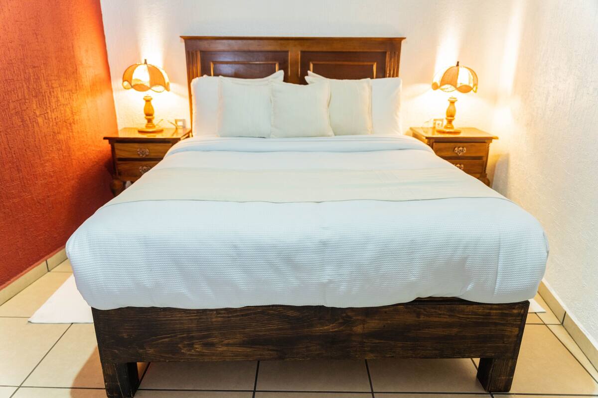 A large bed with a wooden headboard, two bedside tables with lamps, and white bedding.