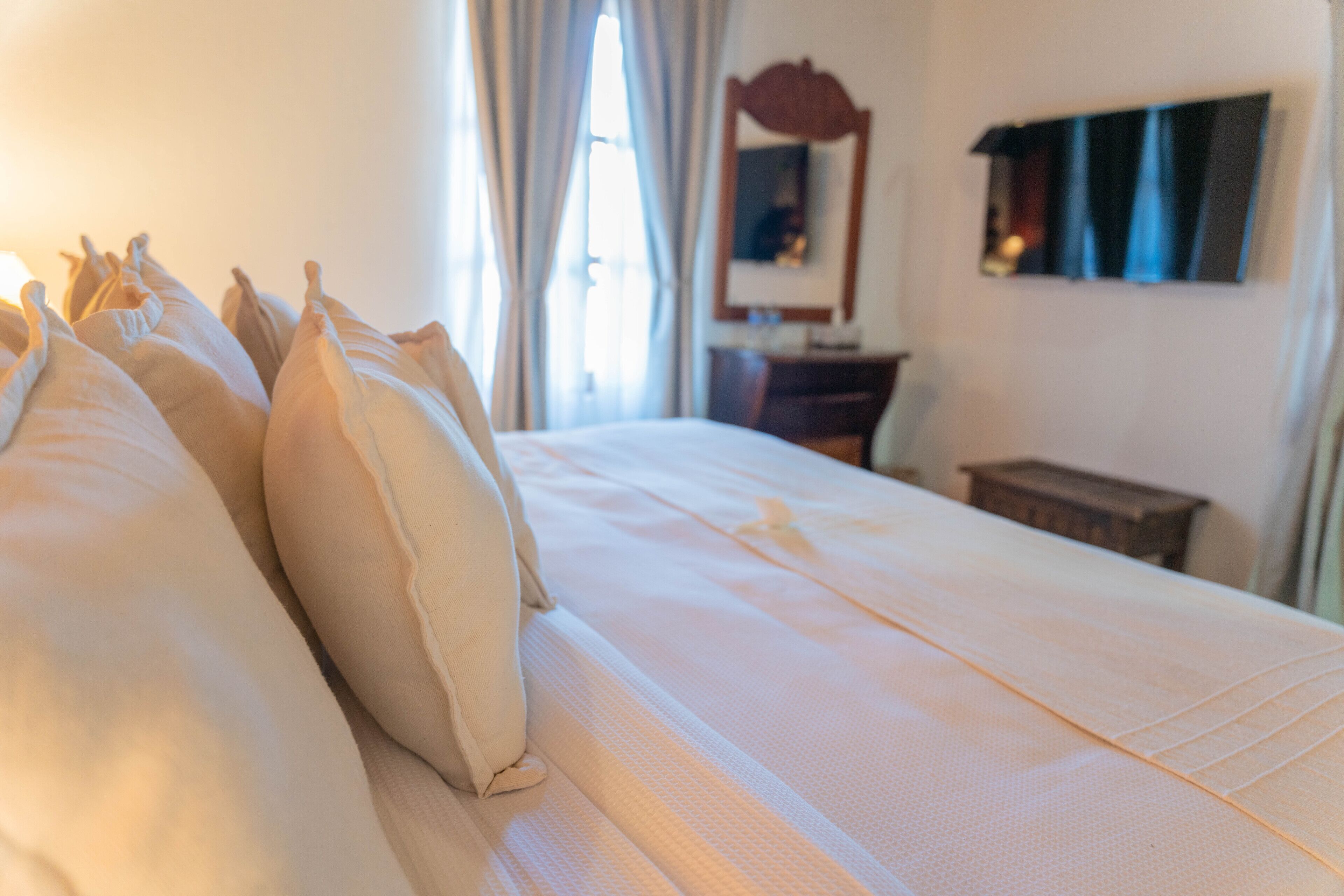 A neatly made bed with pillows, a wooden nightstand, and a mirror on the wall.