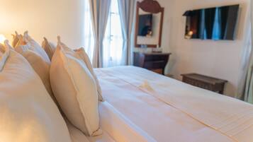 A neatly made bed with pillows, a wooden nightstand, and a mirror on the wall.
