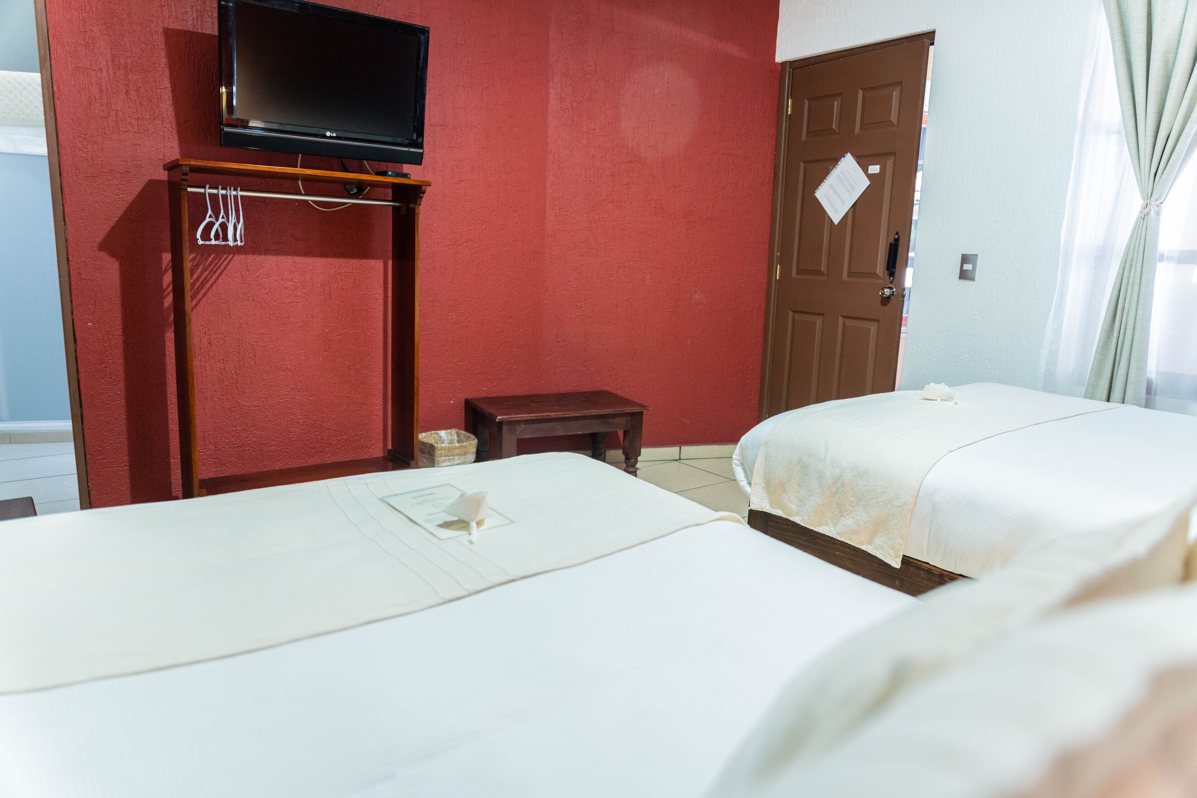 Habitación de hotel con dos camas, un televisor sobre un mueble, una puerta de madera y una mesita.