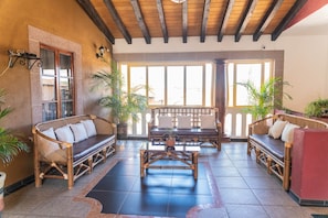 A spacious lobby with a wooden ceiling, large windows, and several seating areas with cushions and plants.