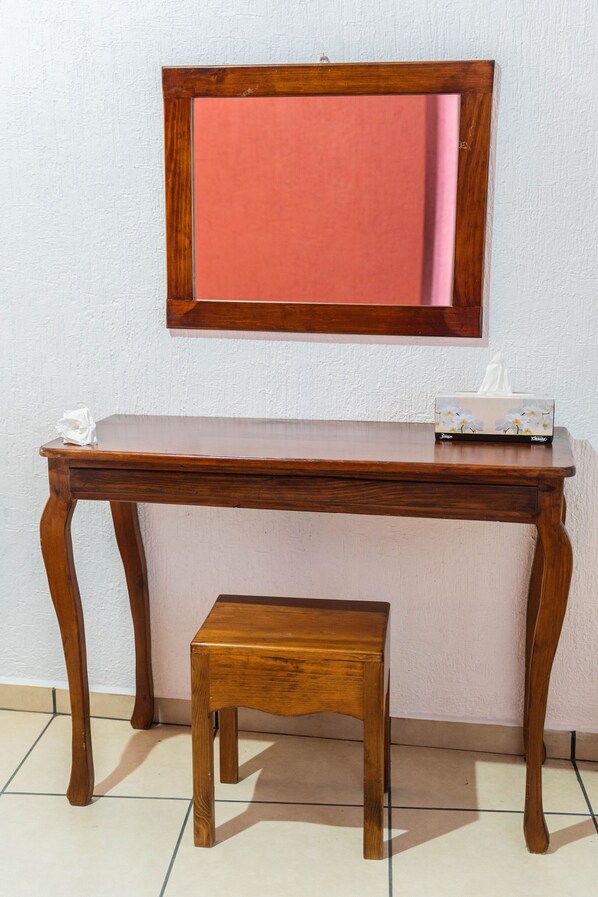 Un escritorio de madera con un espejo encima, una caja de pañuelos y un taburete pequeño al frente.