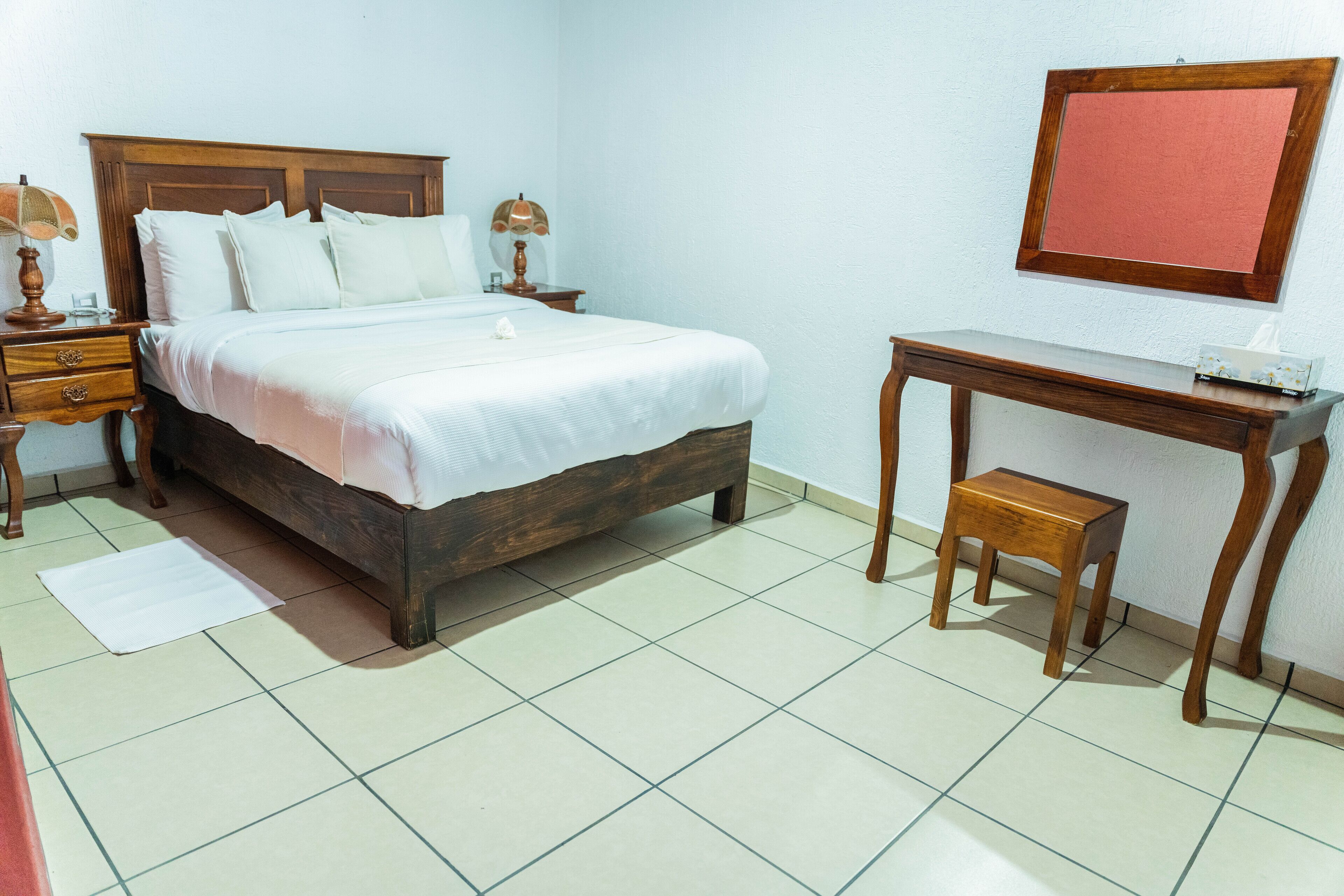 A bedroom with a wooden bed, bedside tables, a desk, and a chair.