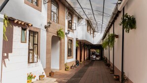 A corridor with white walls, tiled floor, and potted plants. - Casa Graciela Hotel Pátzcuaro (Patzcuaro)