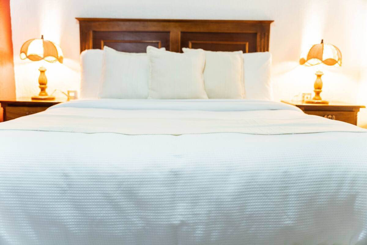 A neatly made bed with a wooden headboard, two bedside lamps, and a white bedspread.