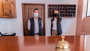 Two individuals standing in a room with a wooden door and a shoe display on the wall. - Casa Graciela Hotel Pátzcuaro (Patzcuaro)