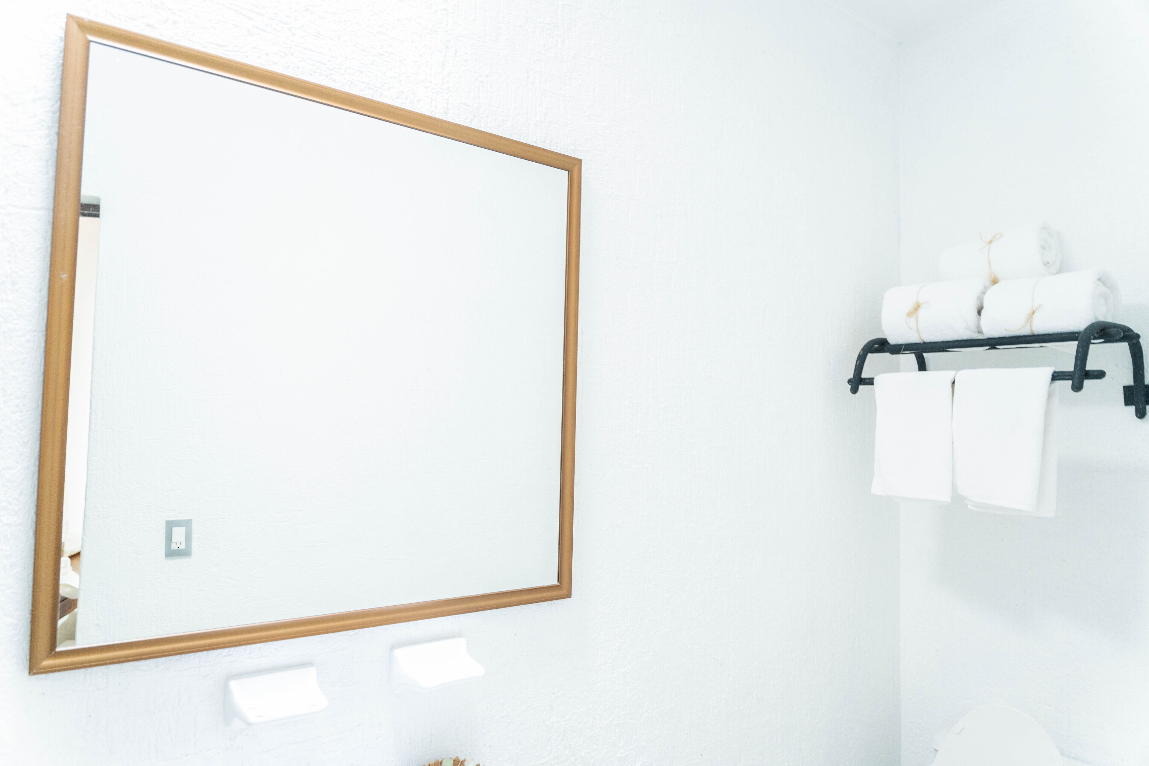 Un baño con un espejo grande, un perchero con toallas dobladas y un interruptor de luz.