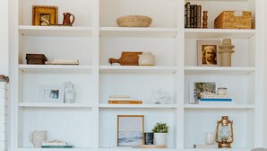A neatly organized living room with a sofa, a fireplace, and a bookshelf filled with various decorative items and books. - Serene Ocean View, Waterfront Cottage Near Olympic National Pk (Port Angeles)