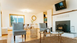A living room with two grey armchairs, a round coffee table, a fireplace, and a TV mounted on the wall. - Serene Ocean View, Waterfront Cottage Near Olympic National Pk (Port Angeles)