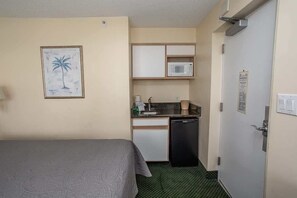 A compact hotel room with a bed, kitchenette, and a door with a lock.