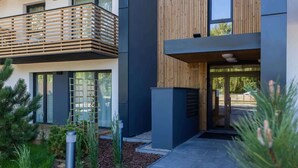 A modern building with a wooden balcony, a dark facade, and a pathway leading to the entrance.