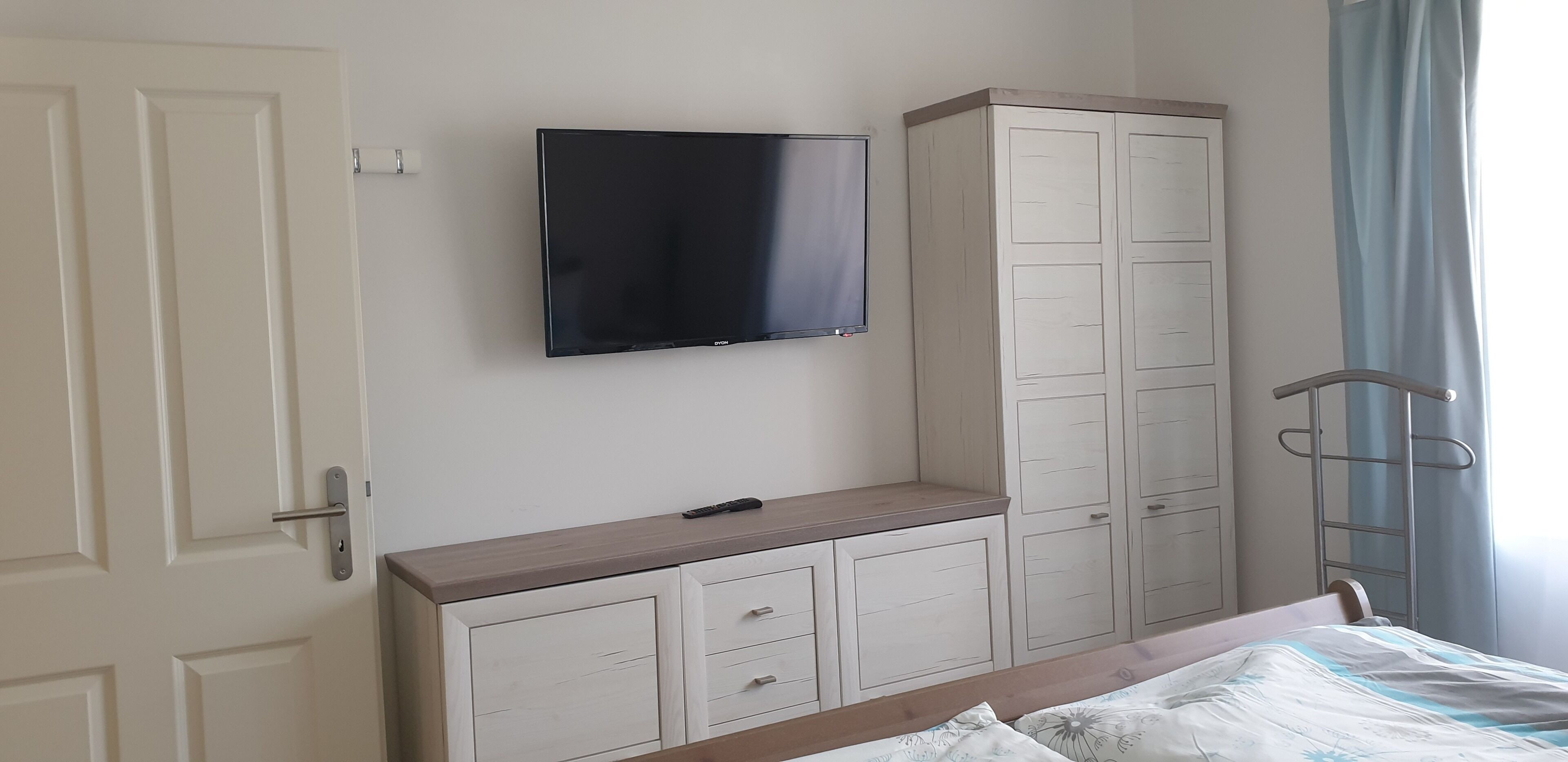 Een slaapkamer met een bed, een aan de muur bevestigde televisie, een kledingkast en een metalen ladder.