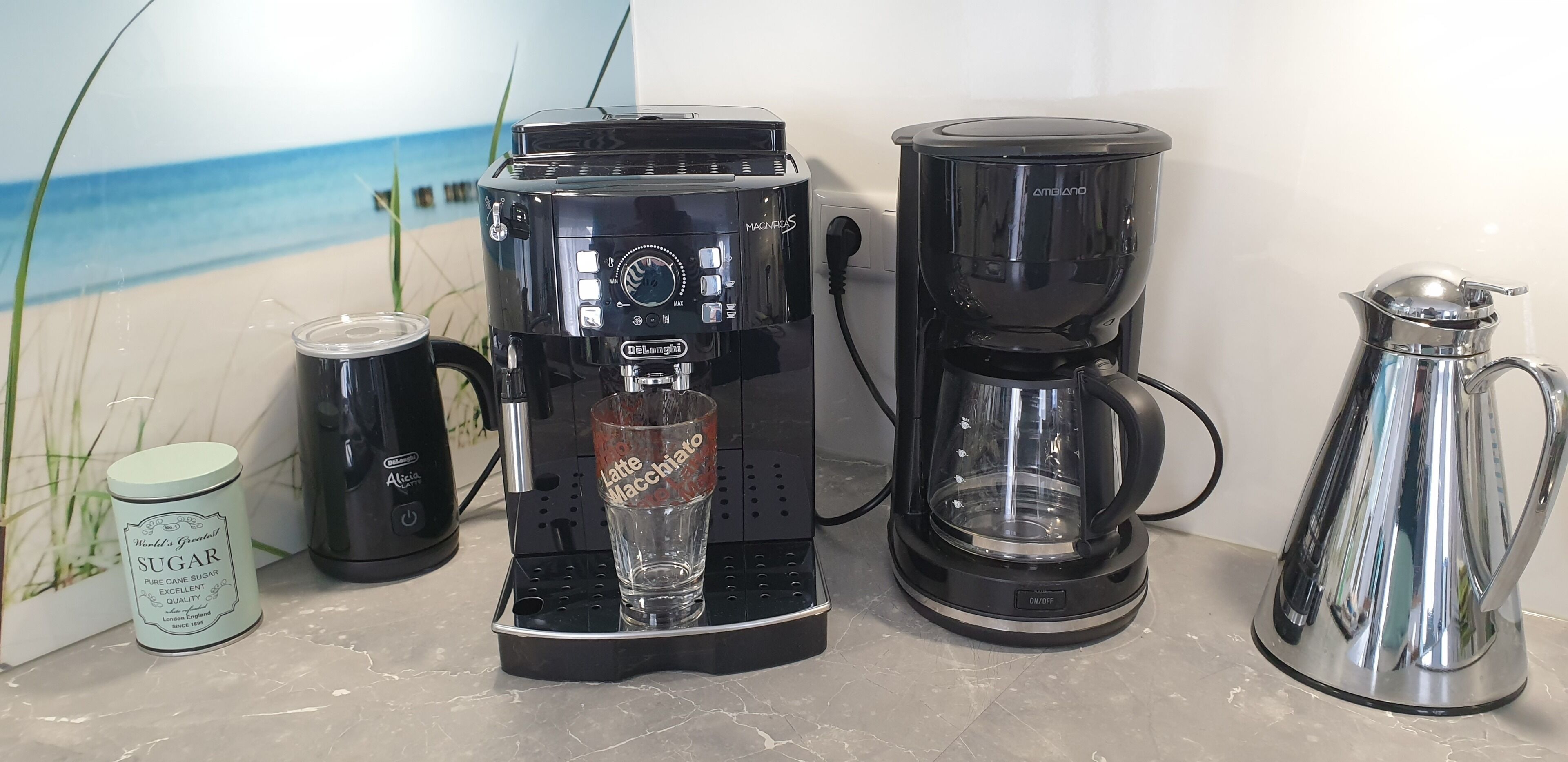 A coffee maker, a glass mug, a thermos, and a sugar container on a countertop.