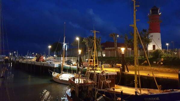 Eine Marina bei Nacht mit vertäuten Booten, einem Leuchtturm und einem Gebäude mit rotem Dach.