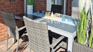 Een terras met een glazen tafel, rieten stoelen en een bakstenen muur.