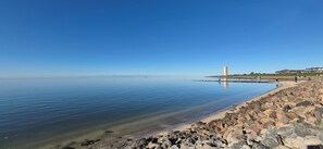 Ett lugnt område vid vattnet med en stenig strand, en klar himmel och en byggnad i fjärran.