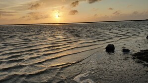 Een strand bij zonsondergang, met golven en een rots op de voorgrond.