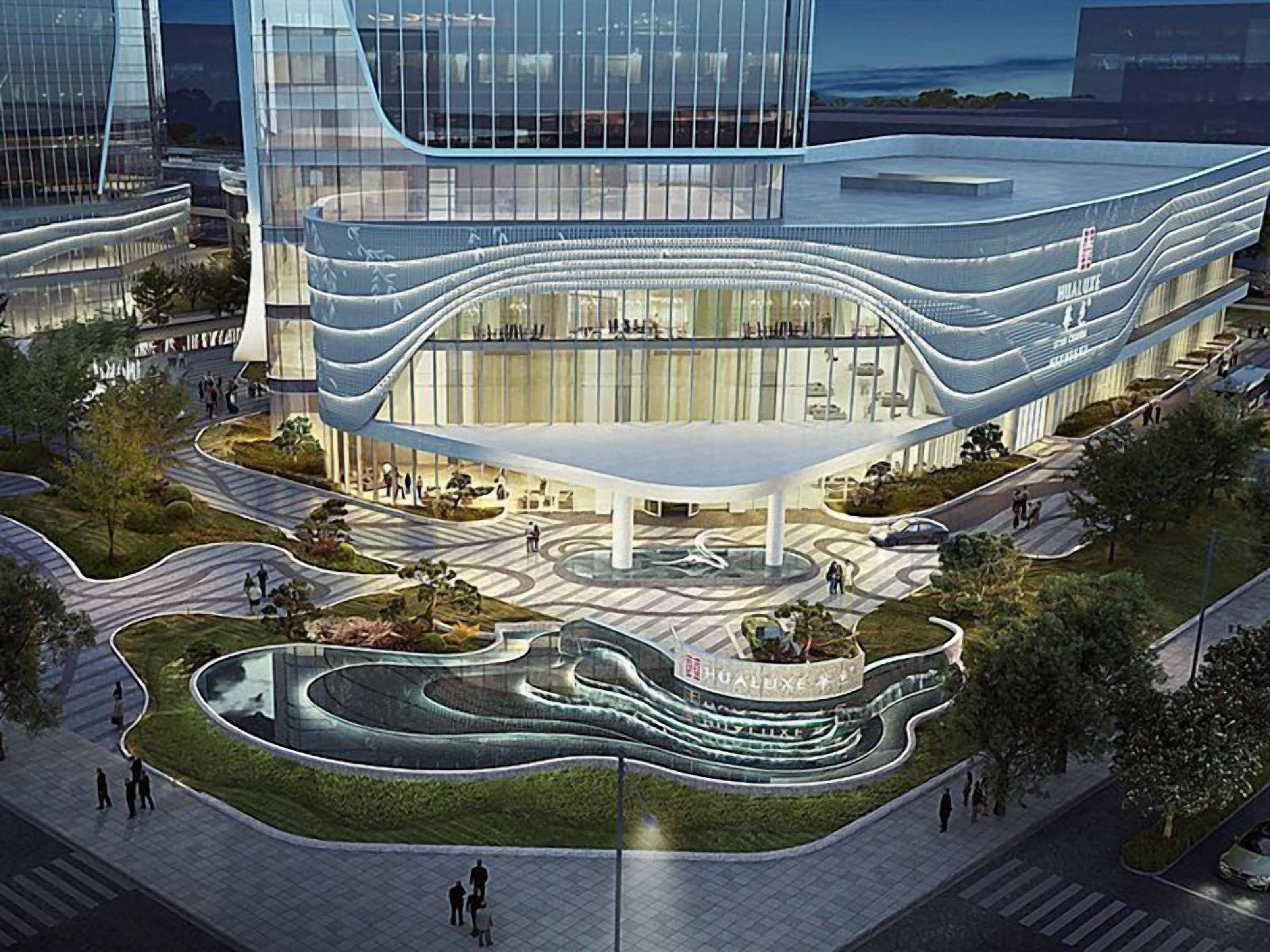 A modern building with a curved facade, a central plaza with a fountain, and surrounding greenery.