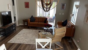 A dining area with a round table and white chairs, a sofa, and a TV in the background. - When Quality & Location Matter (The Villages)