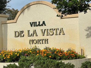 A sign for 'Villa De La Vista North' with a decorative arch and a flower bed in front. - When Quality & Location Matter (The Villages)