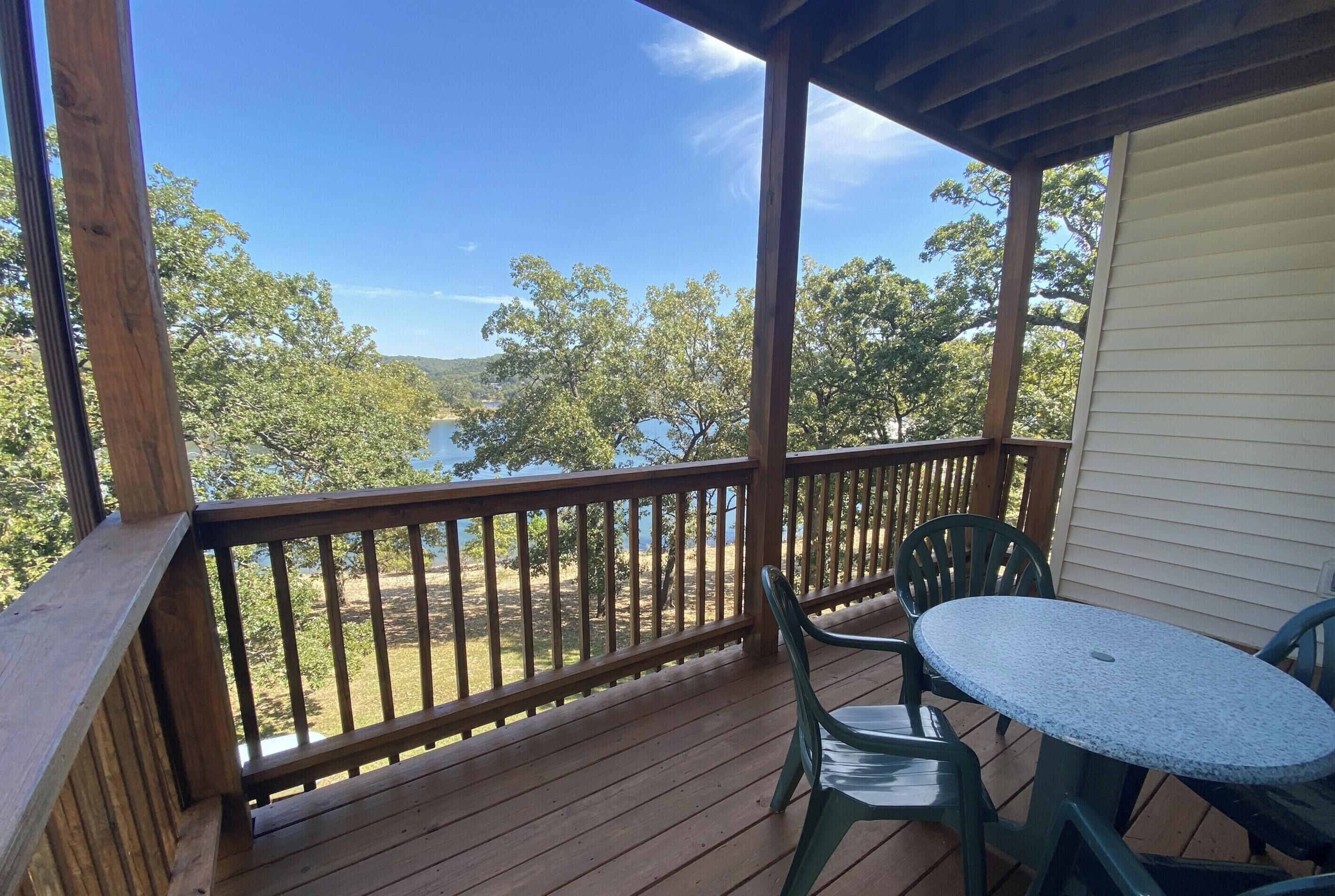 A wooden deck with a table and chairs, overlooking a lake and trees.