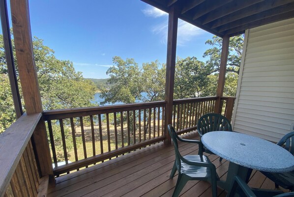 Una terraza de madera con una mesa y sillas, con vistas a un lago y árboles.