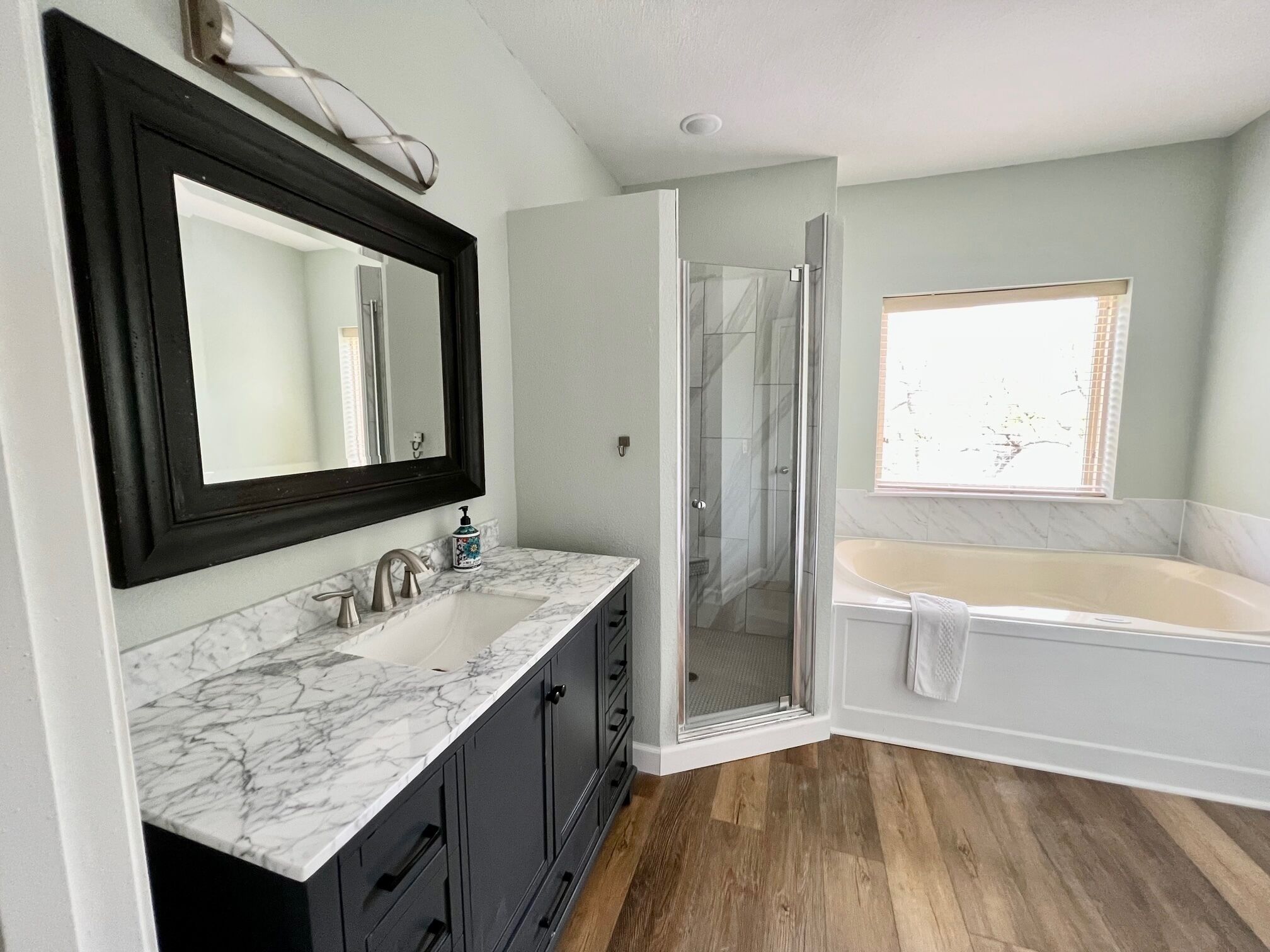 A bathroom with a marble sink, dark cabinets, a glass shower enclosure, and a bathtub.