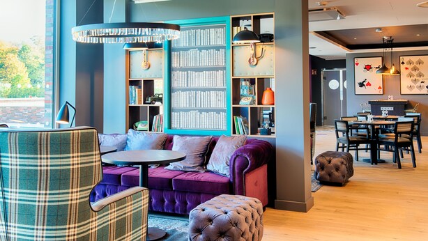 Un salon moderne avec un canapé, un pouf et une bibliothèque.