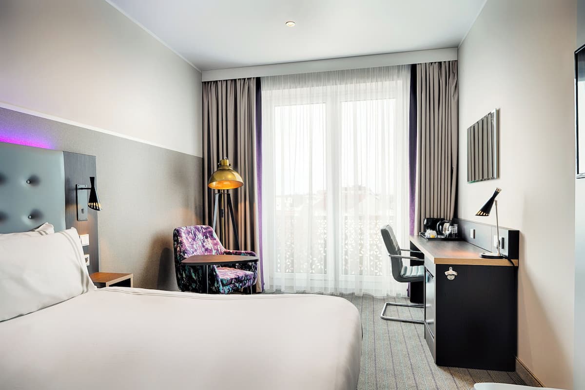 A hotel room with a large bed, a desk with a computer, a chair, and a small table.