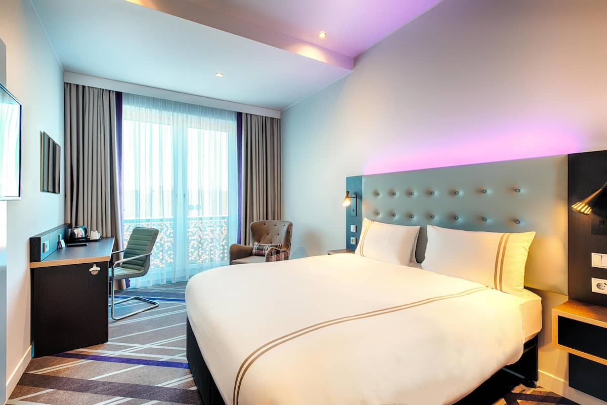 A hotel room with a large bed, a desk, a chair, and a view of the outdoors.