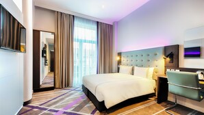 Une chambre d’hôtel moderne dotée d’un grand lit, d’un coin salon, d’une télévision et offrant une vue sur la ville.