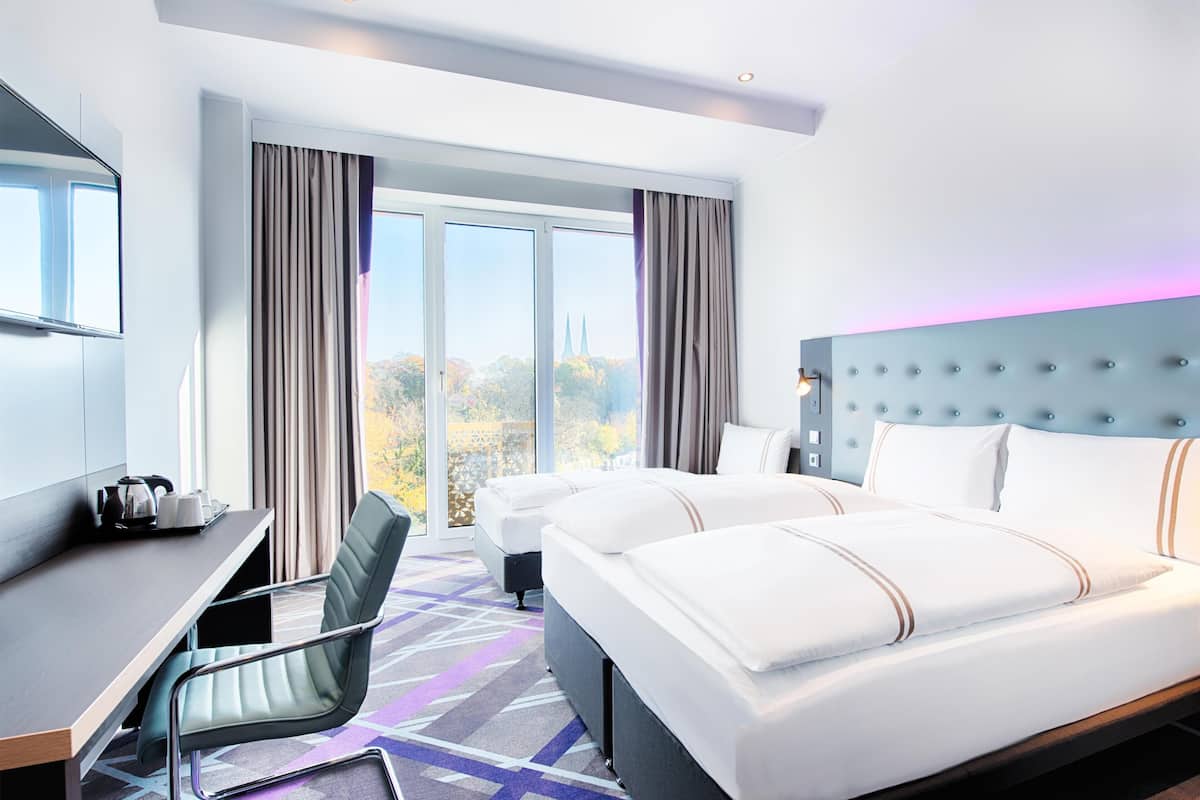 A hotel room with a large bed, a desk with a chair, and a view of a cityscape.