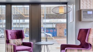 A room with two purple armchairs, a small round table, and a large window with a view of the street. - Premier Inn London Uxbridge Town Centre (Uxbridge)