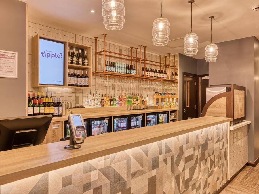 Eine Bar mit digitalen Anzeigen, Flaschenregalen und einer Kasse.