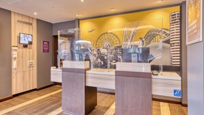 A hotel reception area with a modern design, featuring a large digital display, a glass partition, and a prominent Ferris wheel illustration on the wall. - Premier Inn London Uxbridge Town Centre (Uxbridge)