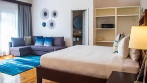 A hotel room with a bed, a sofa, a blue rug, a wardrobe, and a round mirror on the wall.