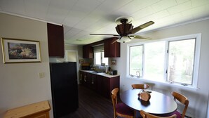 A kitchen with wooden cabinets, a dining table with chairs, a ceiling fan, and a window with a view of greenery. - Beachfront Cabin on Straits of Mackinac  (Mackinaw City)