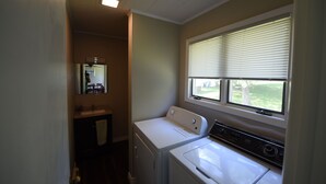 A laundry room with a washing machine and dryer, a window with blinds, and a mirror above the sink. - Beachfront Cabin on Straits of Mackinac  (Mackinaw City)