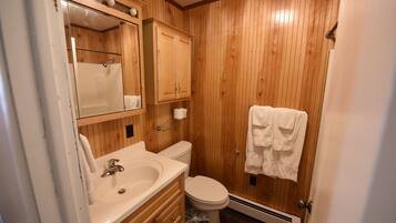 A wooden-paneled bathroom with a sink, mirror, cabinet, toilet, and towel rack.