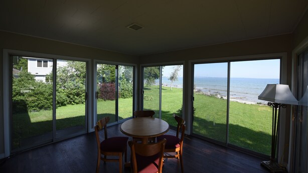 A sunlit room with a round table and chairs, large windows offering a view of the beach and greenery. - Beachfront Cabin on Straits of Mackinac  (Mackinaw City)