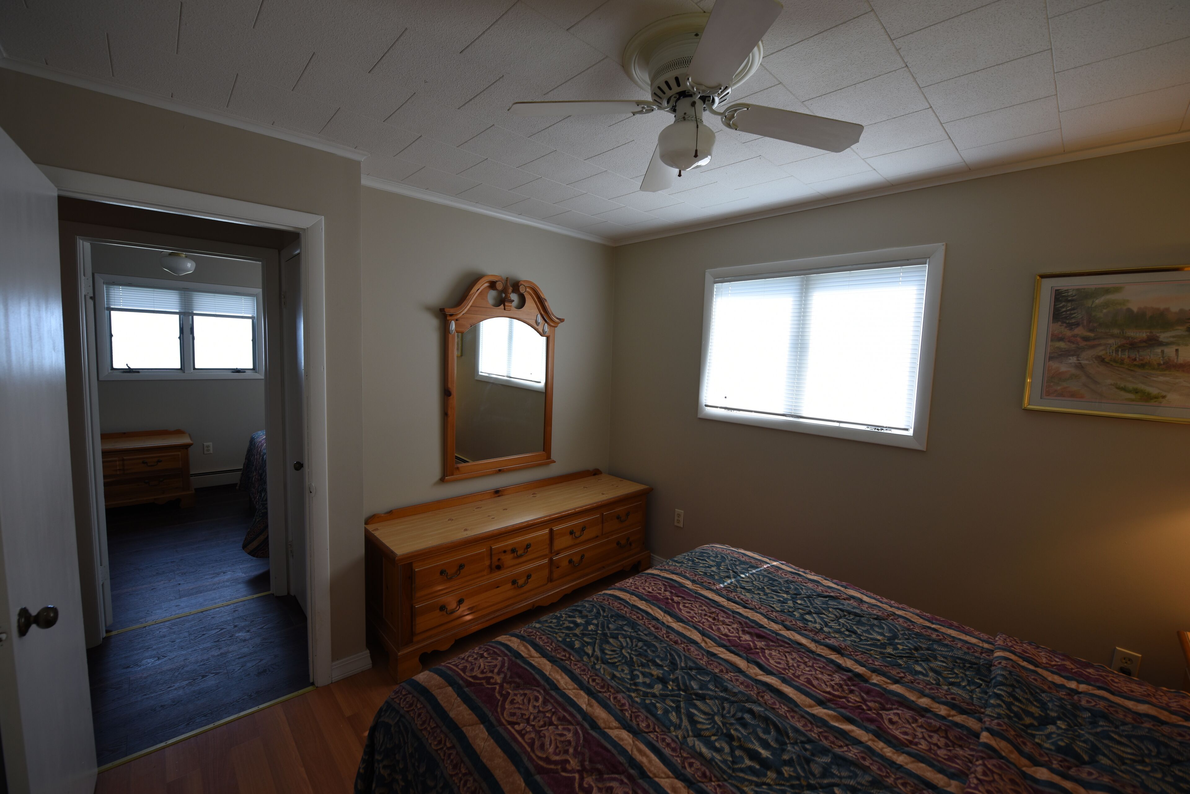 Une chambre à coucher avec un lit, une commode, un ventilateur de plafond et une fenêtre.