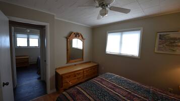 Une chambre à coucher avec un lit, une commode, un ventilateur de plafond et une fenêtre.